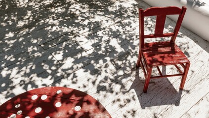 A weathered red chair and polka-dotted table sit on a sun-dappled white patio, shaded by a leafy tree