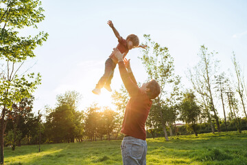 Father tossing his smiling young son into the air and catching him while playing together outdoors...