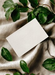 Blank card rests on beige fabric, surrounded by vibrant green leaves;  natural, elegant aesthetic