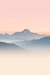 Obraz premium Serene mountain landscape at sunrise with pastel sky and misty layers