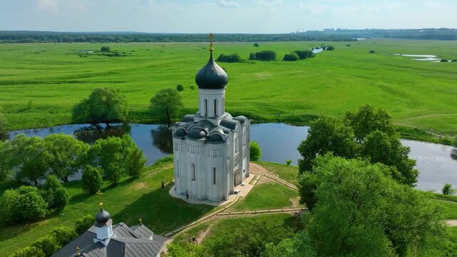 Bogolyubova, Russia - May 13, 2024: A close-up aerial shot of the Church of the Intercession on the Nerl, situated by a tranquil river, with pathways and trees surrounding it