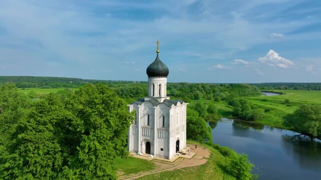 Bogolyubova, Russia - May 13, 2024: A close-up aerial shot of the Church of the Intercession on the Nerl, situated by a tranquil river, with pathways and trees surrounding it