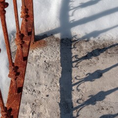 Rusted iron fence detail casts a long shadow on snow-dusted concrete