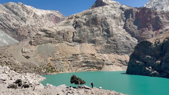 Big Allo lake view with mountain range and turquoise water and a small hiker's silhouette in Fann mountains Pamir Alay Tajikistan