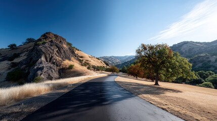 Obraz premium A scenic country road winds through a valley, highlighting contrasting light and shadow, with rugged hills and golden grasses flanking the asphalt.