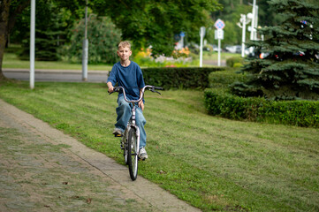 Obraz premium Happy blond teenage boy riding bicycle in sunny summer park, smiling and carefree