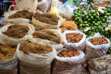 Colorful spices, tobacco leaves, dried fruits and nuts are displayed at stalls in a lively market in Thailand.