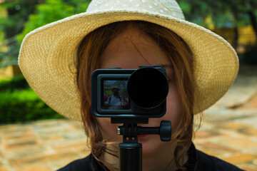 Teenage Latina woman with straw hat filming travel blog with action camera outdoors
