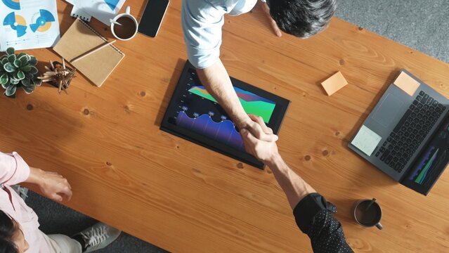 Male leader present financial report to investor and shaking hands while sitting at meeting table. Top aerial view of marketing team with hand shake making agreement or working together. Convocation.