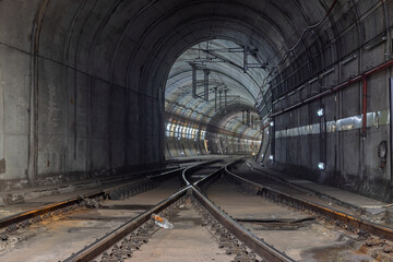 A deep perspective shot of train tracks curving through a long, illuminated concrete tunnel in Rossio, Lisbon. The converging lines and lighting create a powerful sense of an unseen, modern journey.