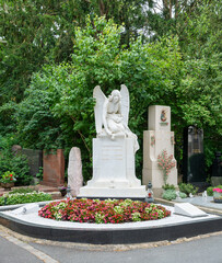 ein Egel kniet auf einem Grabstein davor ein großes Blumenbeet auf einem Friedhof in Würzburg