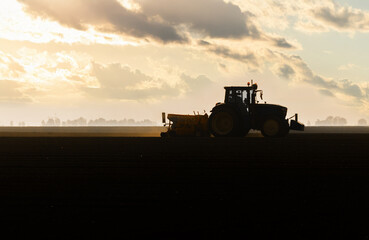 Fototapeta premium Farmer with tractor seeding in sunset