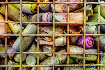 Variety of crushed cans collected in a mesh cage at a recycling facility on a sunny afternoon