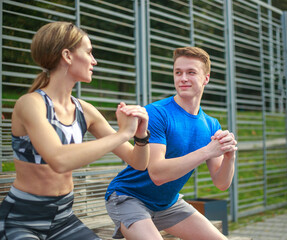 Smiling and joyful couple doing fitness exercises, in city park