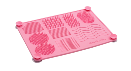 Pink silicone makeup brush cleaning mat with varied textures against a clean white isolated studio background.