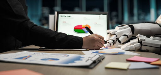 A human hand drawing on paper while a robotic hand assists, showcasing a modern office environment...