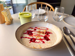 Bowl of oatmeal porridge with raspberry sauce and nuts served in cafe interior. Healthy breakfast, balanced nutrition, and wellness lifestyle