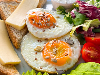 Closeup of fried eggs with seeds, toast, cheese, salad and avocado. Protein, health and fresh breakfast.