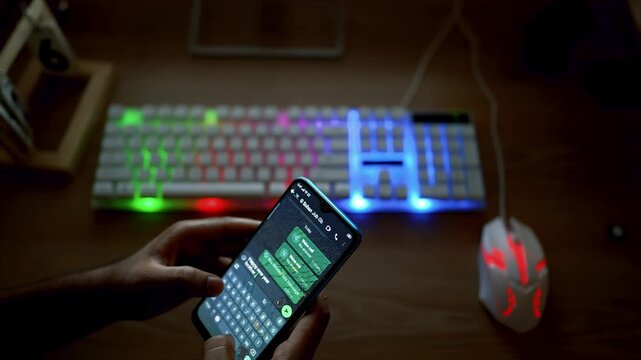 Person using a smartphone with a gaming keyboard and mouse on a desk