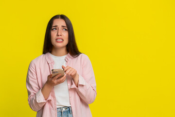 Woman panicking frantically tapping on smartphone screen, reacting in fear after accidentally deleting something important. Girl on yellow background shows emotional stressful gesture of digital panic