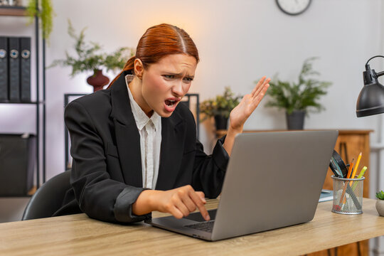 Young businesswoman at home office sees laptop screen freeze slaps table grabs head stressed. Freelancer girl at table hits ctrl alt del waits anxious hoping system recovers soon to keep working again