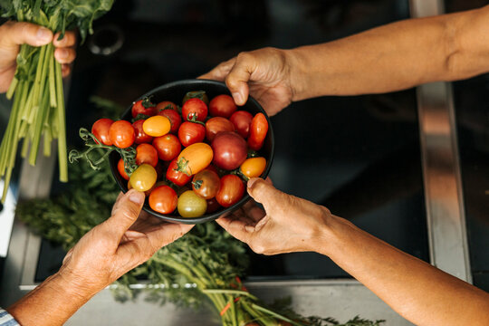 High angle view of woman's hand passing cherry tomato bowl to man