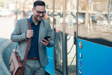 Smiling businessman using smartphone while waiting for bus at bus stop