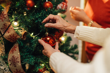 Grandmother hanging christmas ball ornament on christmas tree with family