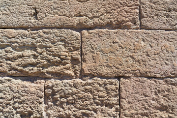 Close-up of a rustic stone wall made of rough, weathered rectangular blocks, creating a textured background in bright sunlight.