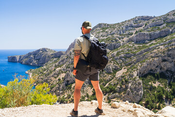 Male hiker with a backpack enjoying the scenic sea view from a cliff top in the Calanques National Park near Marseille.