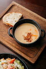 Creamy soup with fried onion topping and rustic bread on wooden tray, cozy lunch concept
