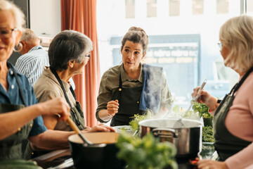Female chef listening to senior woman while teaching in cooking class at commercial kitchen