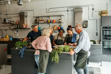 Senior men and women learning from chef in cooking class in cooking class	at commercial kitchen