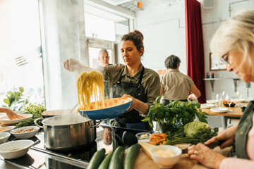 Female chef serving spaghetti in bowl after cooking class in commercial kitchen
