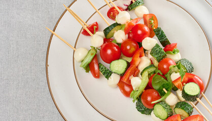 Appetizer of fresh vegetables and cheese on wooden skewers in a plate on the table