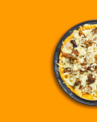 Delicious cheesy pizza with chicken, beef and vegetables served on black plate isolated on white and orange background, tasty fast food, Italian cuisine, restaurant menu and social media food concept