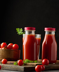Full glass bottle with tomato juice on dark background