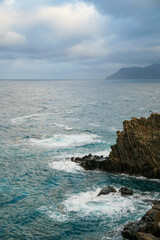 A view of sea waves crashing against a rocky cliff, with another island 