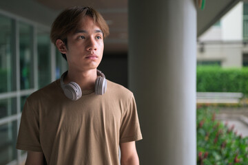 Young Asian Thai man with headphones looking away thinking outdoors