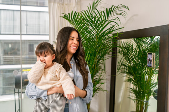Mother holding her baby girl, smiling and creating content at home