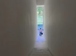 Fotobehang Gang Person walking down a narrow minimalist staircase toward a bright window overlooking a green garden.  © valiantsin