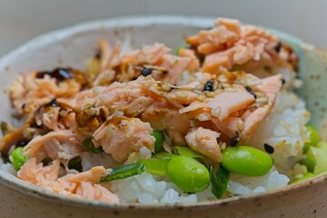 Close up of delicious Salmon teriyaki poke bowl featuring fresh fish, glazed with savory sauce, sprinkled with sesame seeds, alongside steamed rice, edamame beans