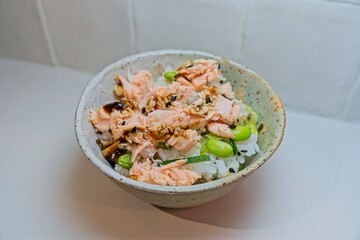 Salmon teriyaki poke bowl featuring glazed fish, sesame sprinkled rice, edamame, presenting nutritious mix of hawaiian and asian inspired cuisine in ceramic serving dish