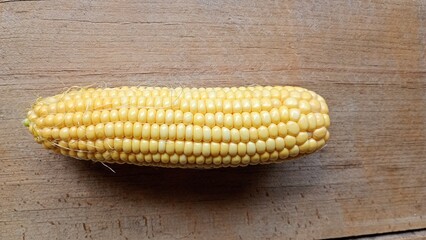  A single ear of ripe corn with its green husk partially peeled back, showcasing vibrant yellow kernels on a rustic wooden background. Captured in a top down view