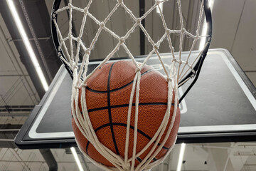 A basketball that hits the basket as it passes through the hoop and into the net. Basketball hoop in a professional basketball arena.