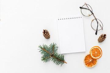 Creative holiday composition with blank notebook mock up, dried orange, glasses and pine cone on white background. To do list, planner and goals concept. Christmas, autumn concept. Flat lay, top view