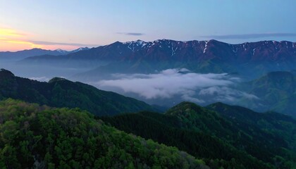 Fototapeta premium A breathtaking vista of mountain ranges bathed in the soft hues of dawn, with layers of misty clouds cascading through valleys.