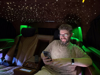 Smiling man using smartphone inside luxury van with star ceiling lights. Digital lifestyle, leisure and premium travel experience.