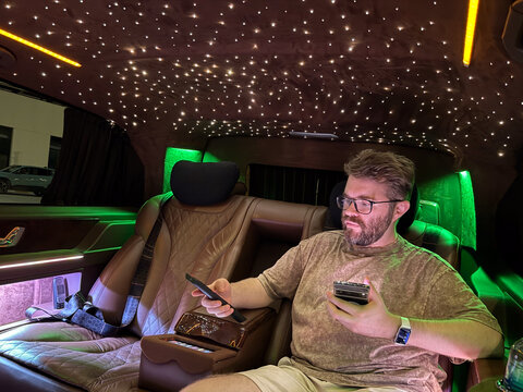 Man focused on smartphone inside luxury illuminated vehicle. Concentration, technology and modern lifestyle in travel environment.