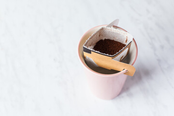 Drip bag in a ceramic cup on windowsill. Instant freshly brewed alternative filter drink in mug. Easy brew black coffee method for home, travel or office. cozy trendy lifestyle